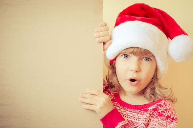 Criança surpreendida segurando o cartão de Natal com a árvore de Natal desenhada. Conceito de férias de inverno