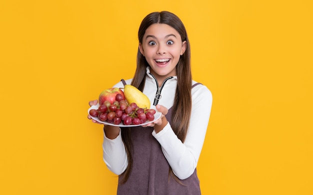 Criança surpresa segura prato de frutas em fundo amarelo