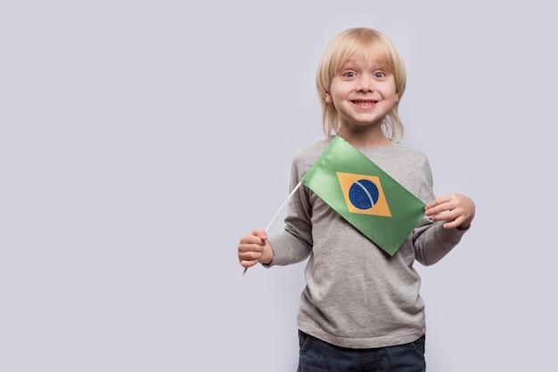 Criança surpresa segurando a bandeira do Brasil Retrato de menino loiro com fundo branco da bandeira do Brasil