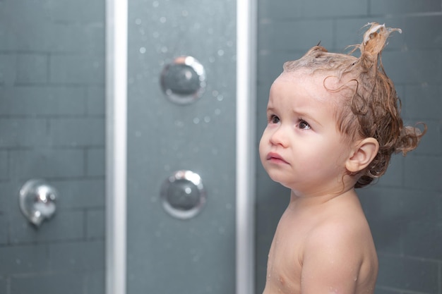 Criança tomando banho Criança engraçada banhada em espuma e lavando na banheira em casa