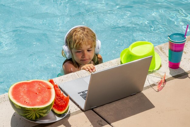 Criança trabalha fora com laptop na piscina Criança trabalhando em laptop da piscina Negócios de verão