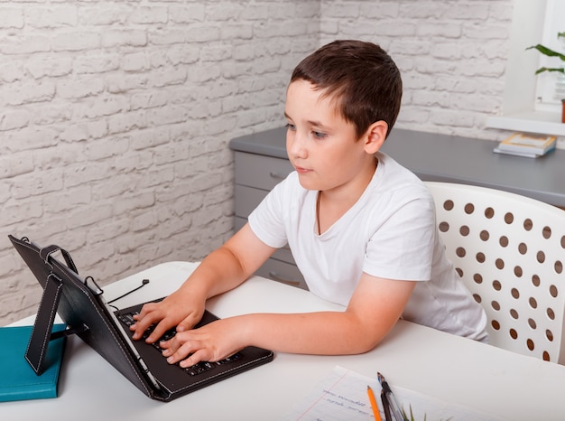 Criança usando um laptop enquanto está sentada em uma mesa