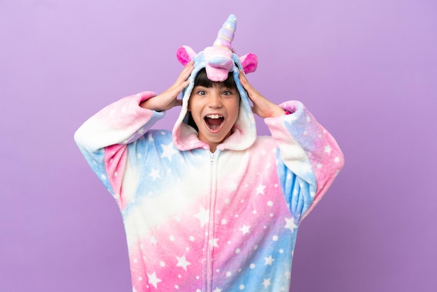 Criança vestindo um pijama de unicórnio isolado em fundo roxo com expressão de surpresa