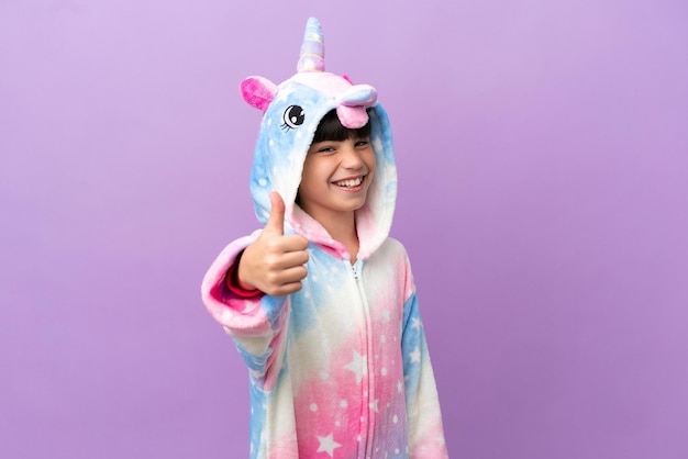 Criança vestindo um pijama de unicórnio isolado em fundo roxo com polegares para cima porque algo bom aconteceu