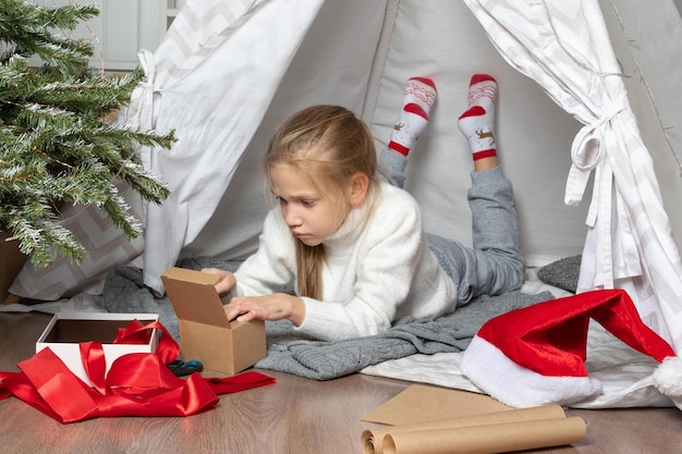 Crianças abrindo presentes de natal menina bonitinha está abrindo um presente e sorrindo enquanto está sentada no chão em casa