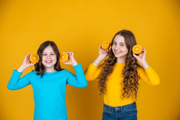 Crianças adolescentes felizes seguram frutas laranja em fundo amarelo
