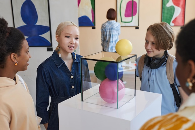 Crianças adolescentes sorridentes olhando para esculturas abstratas na galeria de arte moderna