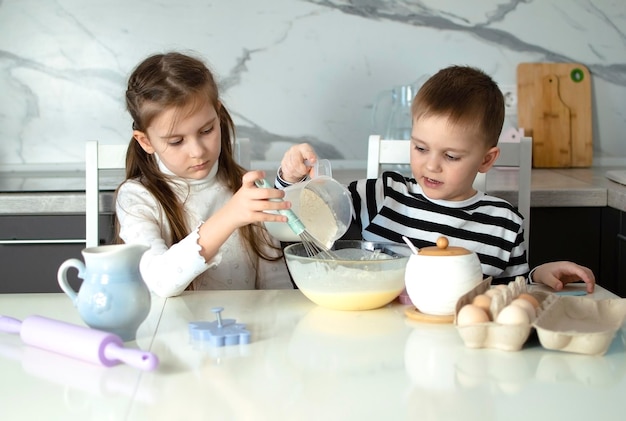 Foto crianças alegres cozinham biscoitos na cozinha branca crianças pequenas gostam de cozinhar na cozinha crianças felizes cozinham massa, cozinham biscos na cozinha as crianças aprendem coisas novas o conceito de lazer das crianças