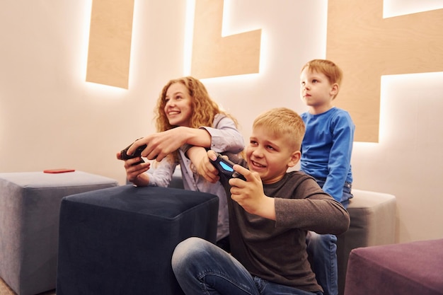 Crianças alegres sentadas dentro de casa e jogando videogame juntos