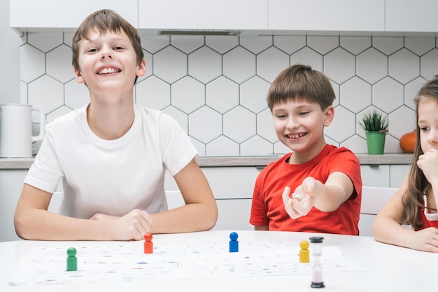 Crianças alegres sorridentes jogando jogo de tabuleiro com peças e dados com limite de tempo Jogo divertido para a família Estratégia educacional