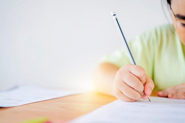 Crianças asiáticas estão estudando exercícios com determinação Ela usa um lápis para escrever em materiais de estudo