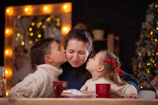 crianças beijando a mãe em uma cozinha decorada de natal