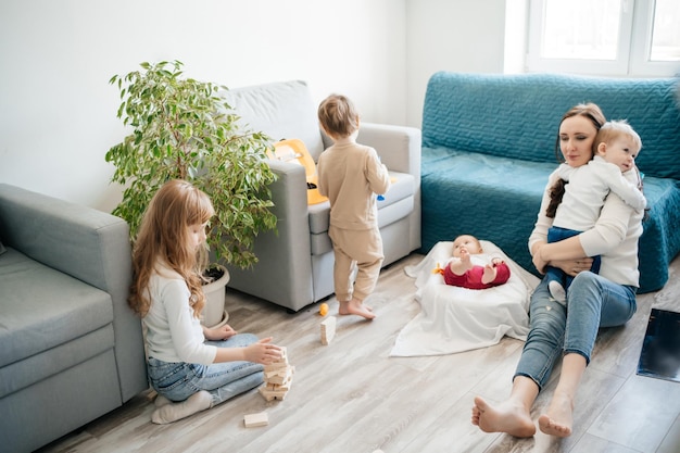Crianças bonitas a brincar em casa com a mãe e o bebé.