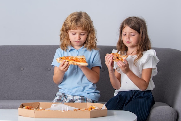 Crianças bonitinhas menino e menina comendo pizza em casa crianças segurando fatias de pizza na festa em ho