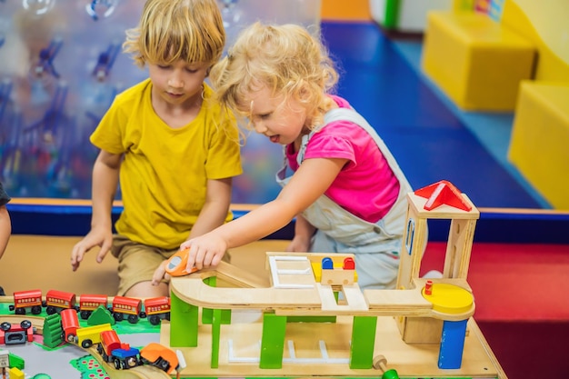 Crianças brincando com trem de madeira criança e bebê brincam com blocos de trens e carros brinquedos educativos para crianças de pré-escola e jardim de infância menino e menina constroem ferrovia de brinquedo em casa ou creche