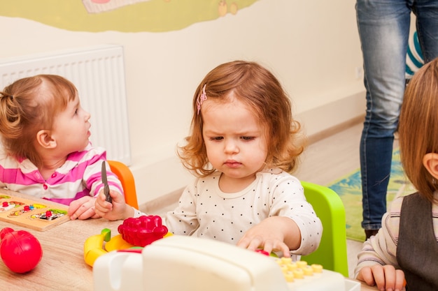 Crianças brincando com utensílios domésticos e frutas artificiais no jardim de infância