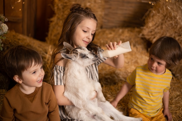 Foto crianças brincando e alimentando cabra com garrafa de leite