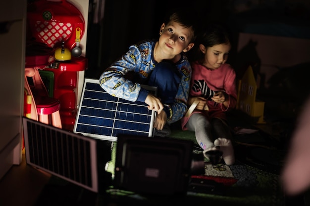 Crianças brincando em casa durante um apagão usando iluminação alternativa com painel solar