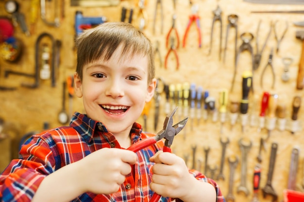crianças, carpintaria, profissão e conceito de pessoas - menino feliz com um alicate na oficina