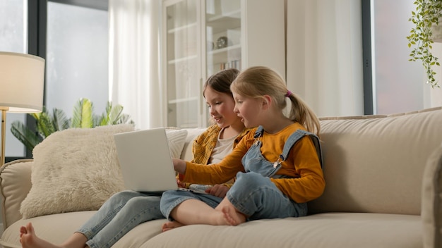 Crianças caucasianas despreocupadas filhas meninas de família vendo filmes divertidos desenhos animados em computador portátil crianças felizes irmãs pequenas conversam amigável jogos de computador conversando online sofá em casa