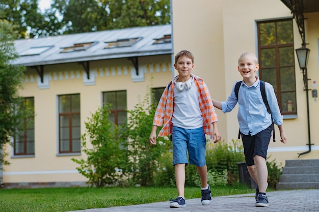 Crianças caucasianas felizes fugindo da escola com mochilas em dia ensolarado Início do ano acadêmico Meninos rindo de tolo