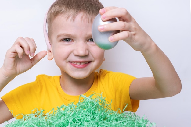 Crianças celebram a Páscoa Uma criança engraçada em orelhas de coelho está procurando ovos de Páscoa em papel verde imitando grama