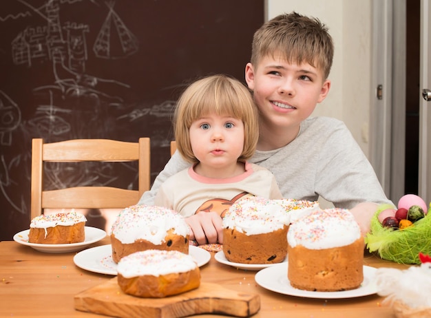 Crianças com bolos caseiros tradicionais de Páscoa e ovos coloridos Menino adolescente e uma menina sentada à mesa cheia de bolos tradicionais de Páscoa Conceito de férias de Páscoa