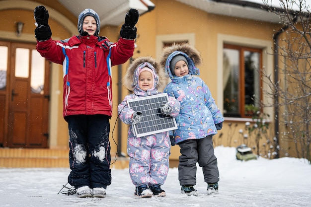 Crianças com painel solar contra casa no inverno Conceito de energia alternativa
