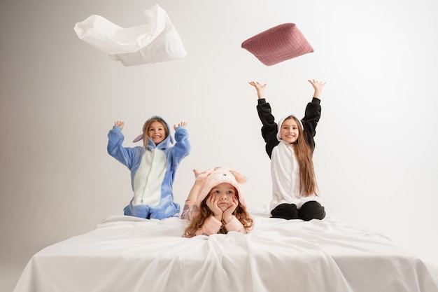 Crianças com pijamas macios e quentinhos brincando em casa, brigando com os travesseiros. garotinhas se divertindo, festejando, rindo juntas, parecem elegantes e felizes. conceito de infância, atividade de lazer, felicidade.