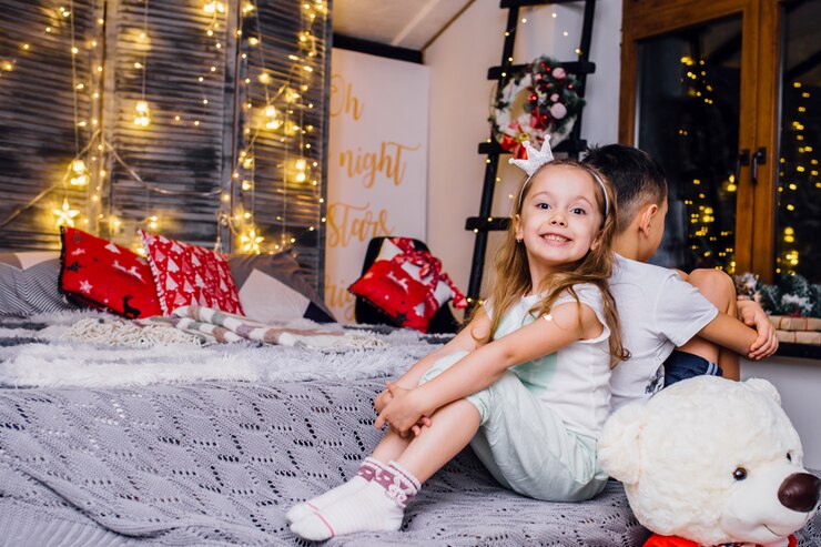 Crianças com ursinho sentado em uma sala moderna decorada sob o motivo de Natal com presentes, copos, iluminação, abeto e neve