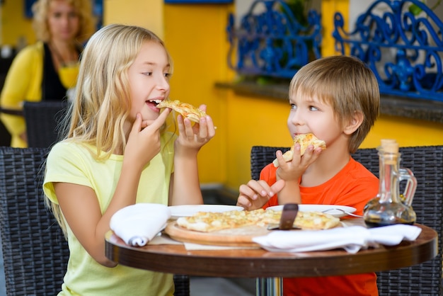 Crianças comem pizza e bebem suco ao ar livre
