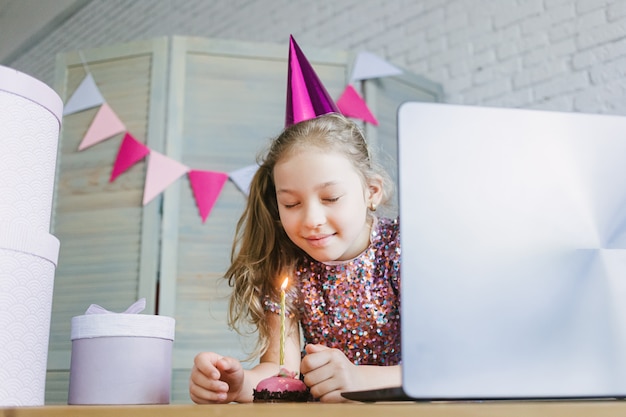 Crianças comemorando seu aniversário por meio de festa virtual de videochamada com amigos. Acende uma vela.