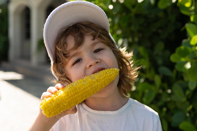 Crianças comendo milho Garotinho de chapéu come milho na espiga no jardim Conceito de cultivos agrícolas e de outono