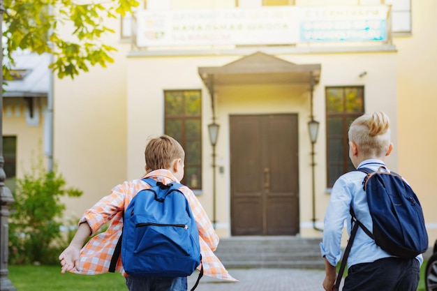 Crianças correndo para a escola com mochilas em dia ensolarado Início do ano letivo Meninos à porta da escola