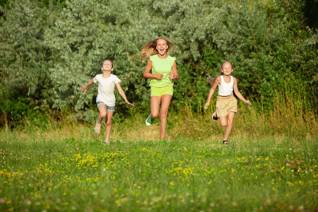 Crianças, crianças correndo no pasto ao sol do verão. Pareça feliz, alegre, com emoções brilhantes e sinceras. Bonitos meninos e meninas caucasianos. Conceito de infância, felicidade, movimento, família e verão.