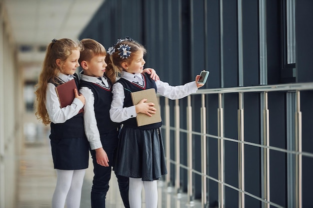 Crianças da escola de uniforme junto com telefone e fazendo selfie no corredor Concepção de educação