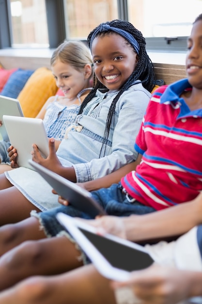 Crianças da escola sentado no sofá e usando tablet digital na biblioteca