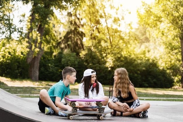 Crianças da moda com pranchas de skate e penny se comunicam e discutem no playground esportivo conceito de amizade de meninos e meninas crianças sorriem e riem e se divertem juntos