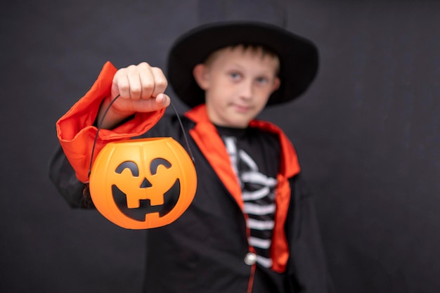 Foto crianças de halloween um menino em uma fantasia de esqueleto segura uma lanterna de jack o fundo preto copiar espaço uma criança em um chapéu de casaco preto segura uma abóbora de halloween lugar para texto