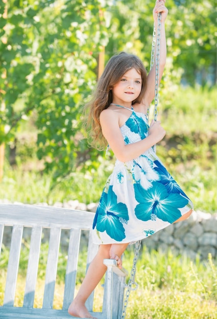 Crianças de moda vestem criança feliz menina em um baloiço no parque de verão crianças sonhadoras rosto pequeno