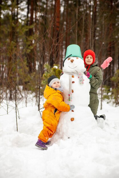 Crianças de nove e três anos no inverno caminham perto do boneco de neve