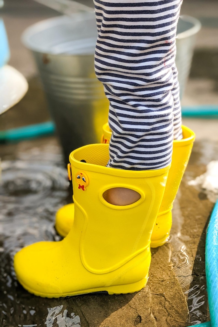 Foto crianças de pés em botas de chuva de borracha amarela na água em um dia chuvoso