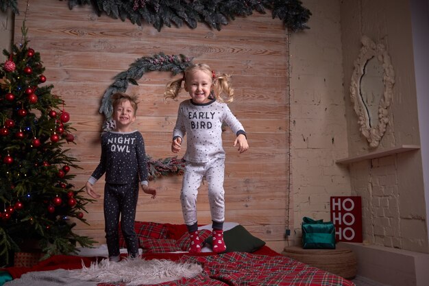 Crianças de pijama brincando em casa na noite de feriado de natal. criança feliz pulando na cama.