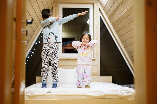 Crianças de pijama macio e quente brincando na casa da cabana de madeira Conceito de felicidade na atividade de lazer infantil Irmão e irmã se divertindo e brincando juntos