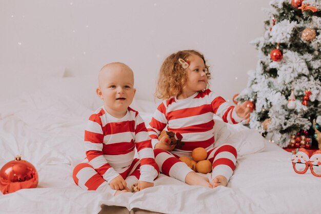 Crianças de terno vermelho e branco comem tangerinas na cama irmão e irmã comemorando o Natal