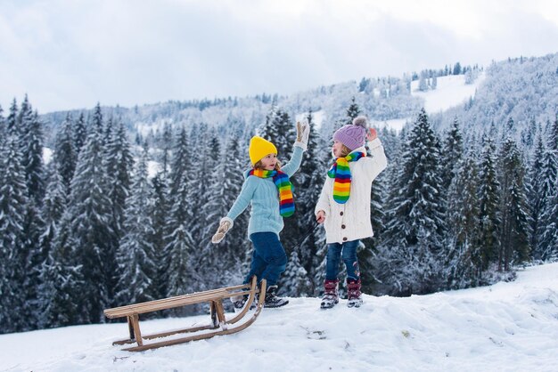 Crianças de trenó montando um trenó crianças filho e filha brincando na neve no inverno ao ar livre crianças divertidas