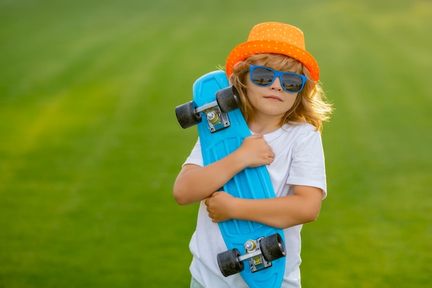 Crianças de verão, infância e moda, criança fofa com skate no fundo do parque de verão, garoto engraçado