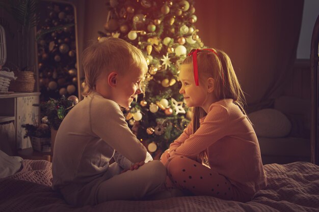 Crianças deitam-se na cama no contexto de uma árvore de Natal. Decorações de Natal, esperando o feriado.