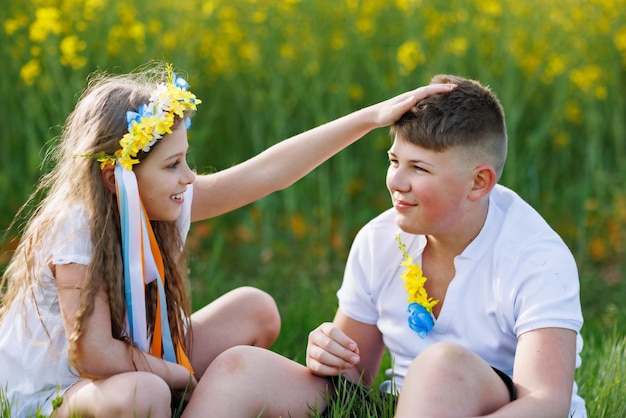 Crianças desfrutando do tempo, irmão e irmã, sentam-se em agachamentos e conversam no campo com flores e grama sob o céu