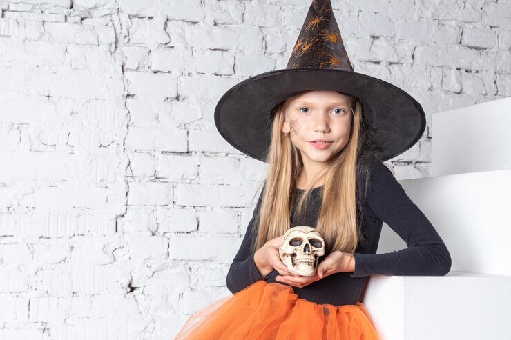 Foto crianças do halloween uma garotinha loira sorridente em uma fantasia de bruxa segurando uma caveira de brinquedo sentada nos degraus da casa